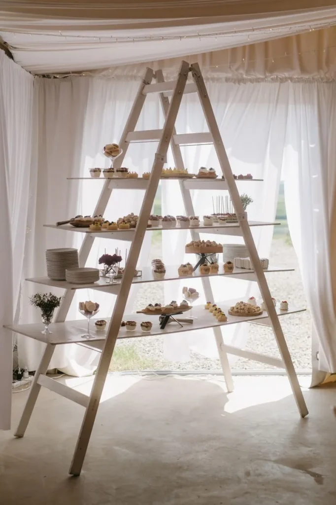 Originální sweet bar na svatbu uspořádaný na bílém žebříku se sladkými dezerty a cupcakes.