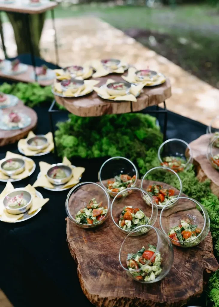Moderní venkovní catering na dřevěných podnosech s mechem, nabízející například čerstvé saláty v miskách pro hosty.